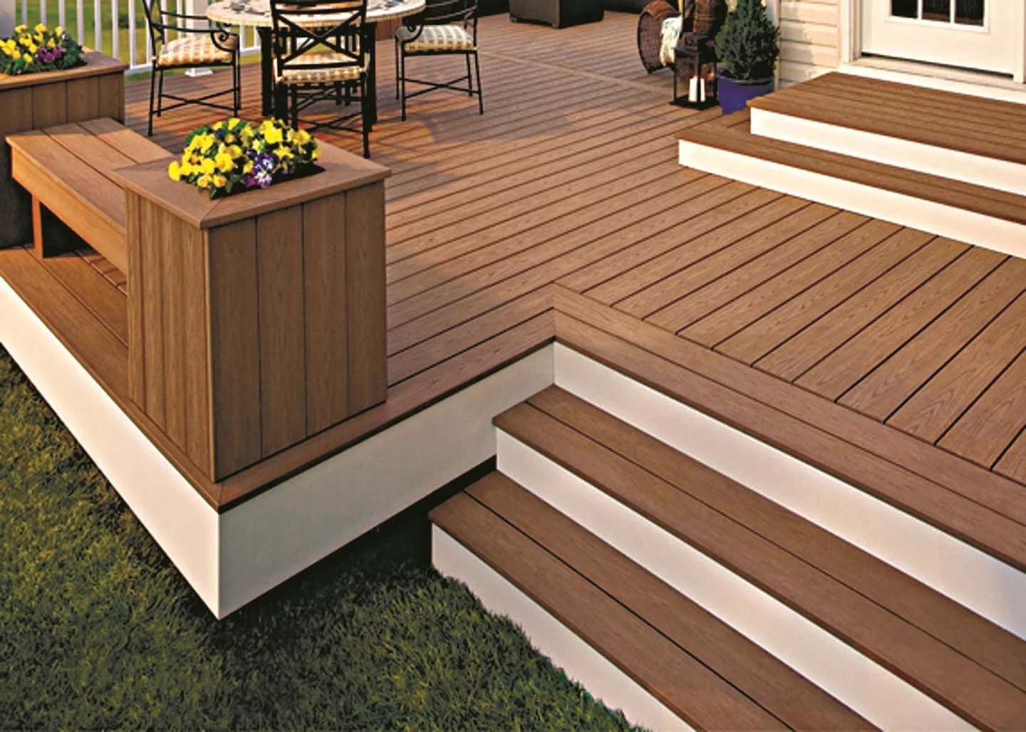 A multi-level composite deck with warm brown planks, white risers on the steps, and built-in benches and planters, leading to an outdoor dining area.