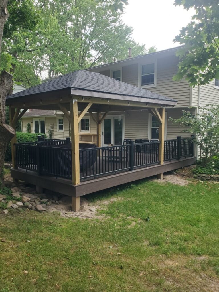 A stunning covered deck in Rochester NY featuring dark composite decking, black railings, and a custom wooden gazebo or pavilion, built by an expert outdoor living contractor.
