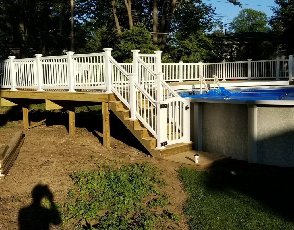 An elevated wood deck in Rochester NY with white vinyl railings and a safety gate surrounds an above-ground pool, expertly built by a local deck contractor.