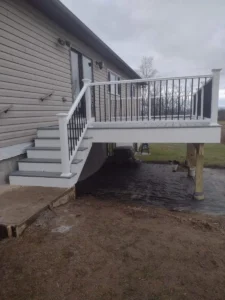 Elevated light grey composite deck in Rochester NY with white posts, black balusters, and matching stairs, attached to a house; built by Rochester deck builders