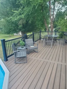 "Furnished composite pool deck in Rochester NY featuring brown Trex decking, black aluminum railings, and outdoor seating, built by local deck builders.