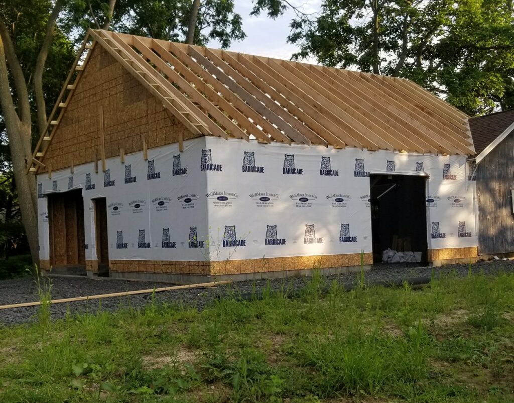 Rochester, NY builder working on a substantial outbuilding, featuring wooden roof structure and 'Barricade' building wrap