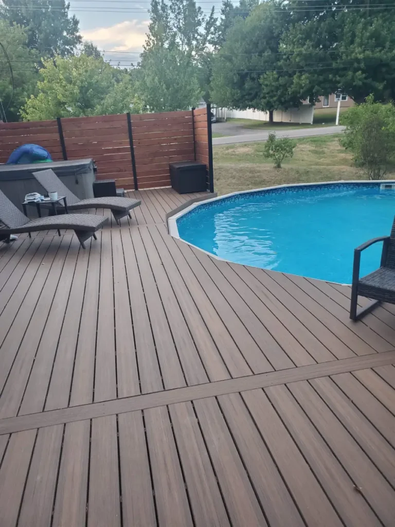 Spacious composite pool deck in Rochester, NY, with light brown decking, surrounding an above-ground pool, featuring a hot tub and privacy fence.