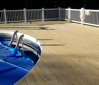 A spacious light-colored wood deck in Rochester NY with white vinyl railings surrounding an above-ground pool, built by a professional deck builder.