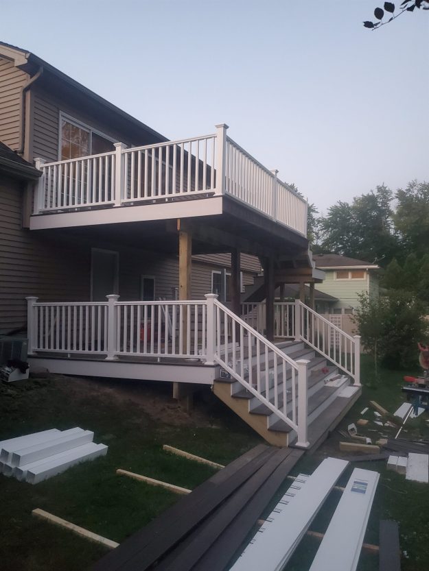 A large multi-level composite deck in Rochester NY featuring grey decking, white vinyl railings, and multiple staircases, shown during the final stages of construction by a local deck builder.