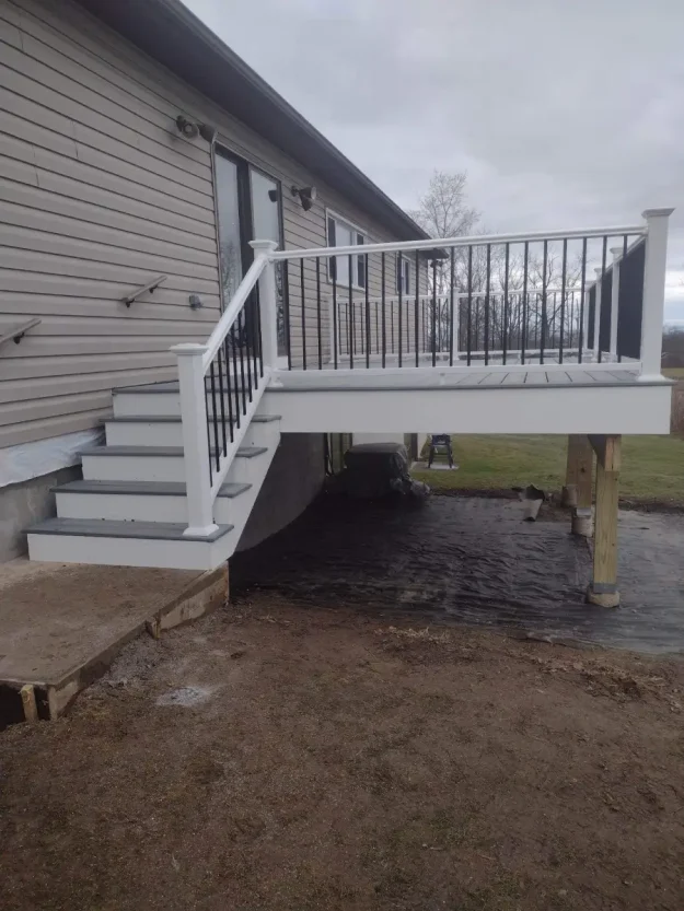 Elevated light grey composite deck in Rochester NY with white posts, black balusters, and matching stairs, attached to a house; built by Rochester deck builders