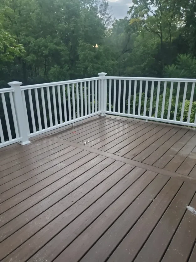 Brown composite deck with white vinyl railings in Rochester, NY, offering a view of a lush treeline.