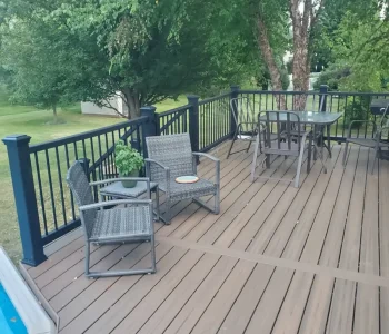 "Furnished composite pool deck in Rochester NY featuring brown Trex decking, black aluminum railings, and outdoor seating, built by local deck builders.